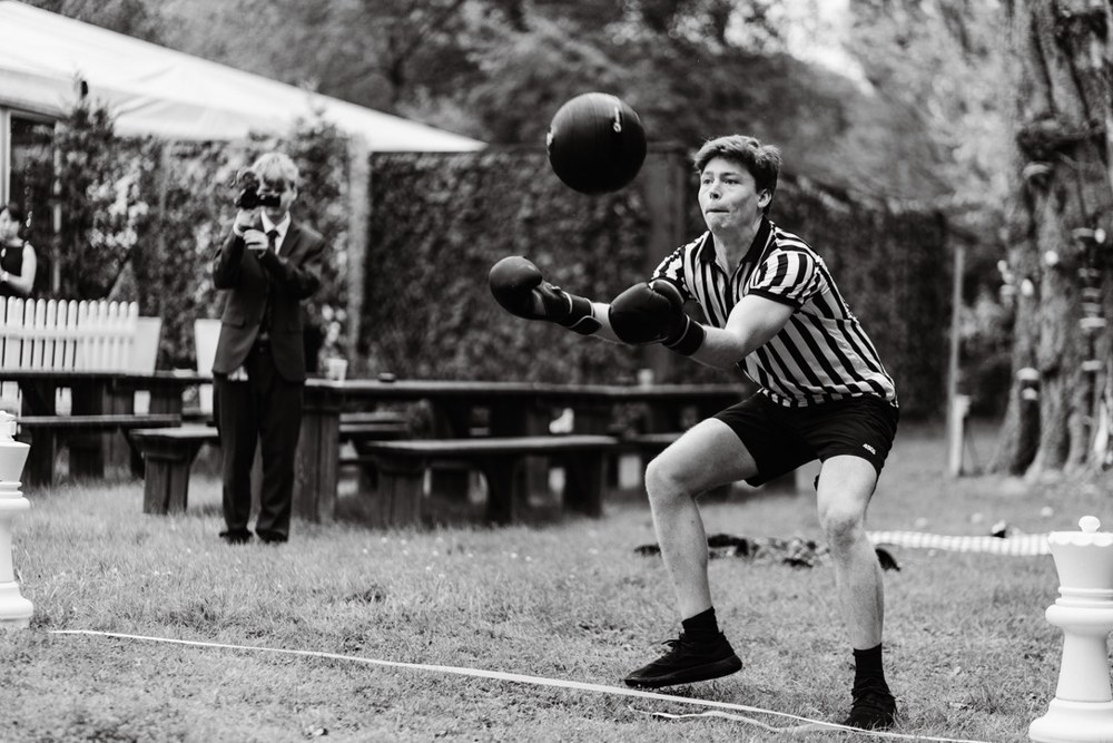 Brenton in a referee shirt and boxing gloves, catching a medicine ball mid-flight